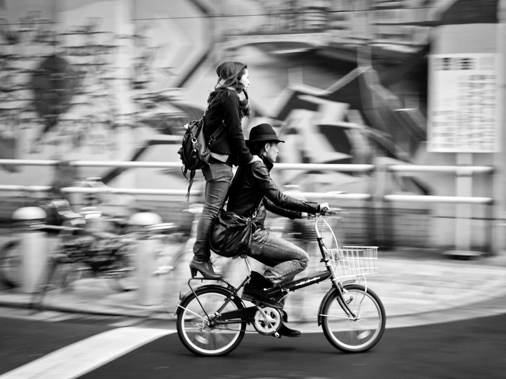 Picture of a man and woman riding a bicycle down a city street in Japan